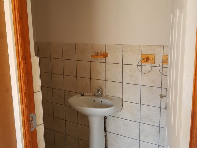 A compact guest bathroom featuring a pedestal basin and tiled splashback, currently in need of cosmetic updates.