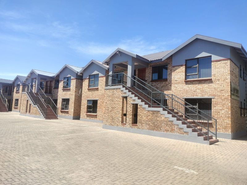 A multi-unit residential building featuring face brick construction, external staircases with metal railings, and a paved driveway area.