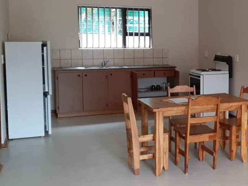 Open-plan kitchen and dining area featuring basic cabinetry, tiled splashback, and security bars on the window.