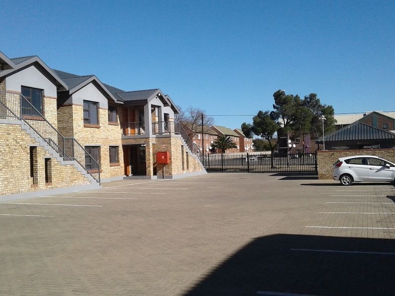 Exterior view of a multi-unit residential complex featuring face brick construction, paved parking area, and external metal staircases.