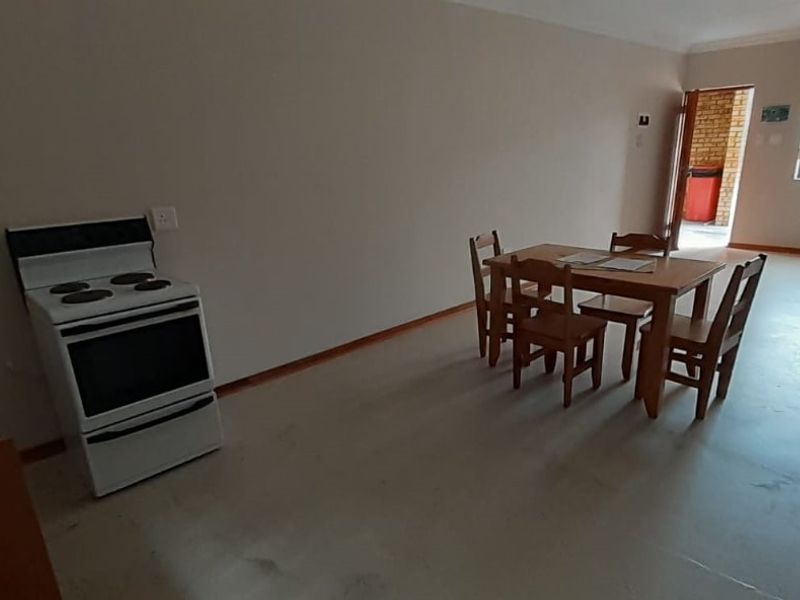 Open plan living and kitchen area featuring a freestanding stove, large window with security bars, and neutral wall finishes.