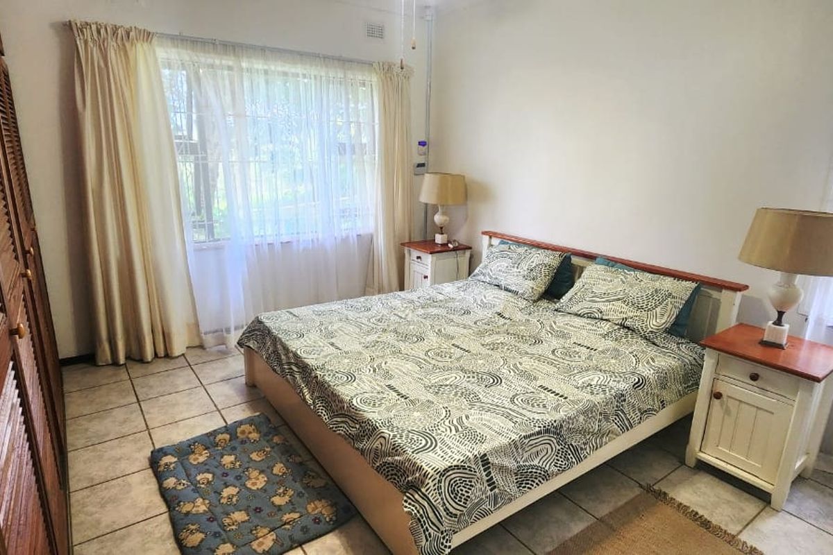 A bedroom featuring tiled flooring, built-in wooden louvered cupboards, and windows fitted with security bars.