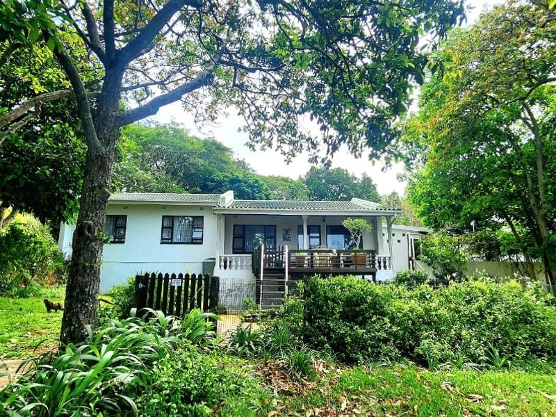 A rear view of the house featuring a timber deck, sliding doors, and a lush, mature garden setting.