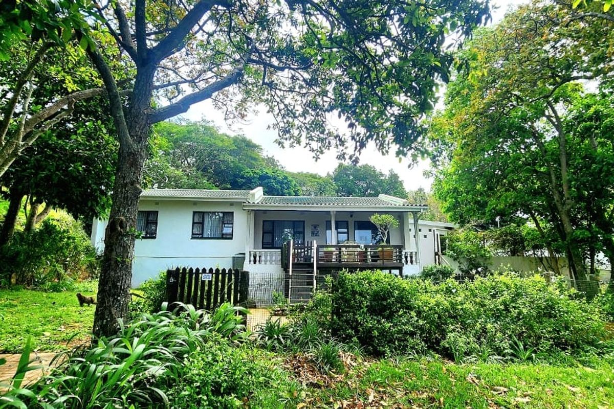 A rear view of the house featuring a timber deck, sliding doors, and a lush, mature garden setting.
