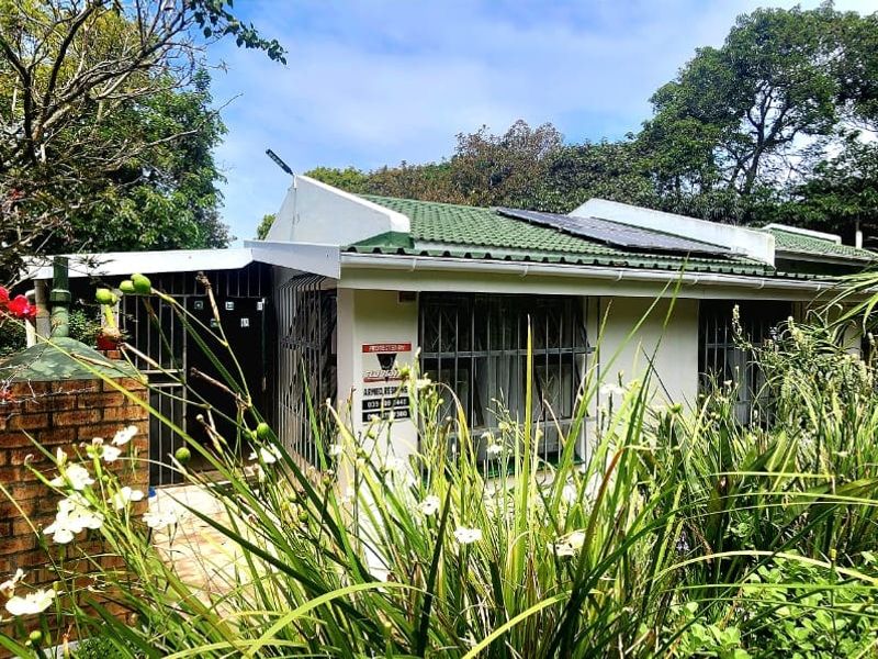 Front elevation of a residential house featuring a tiled roof with solar panels, security gates, and established garden surroundings.