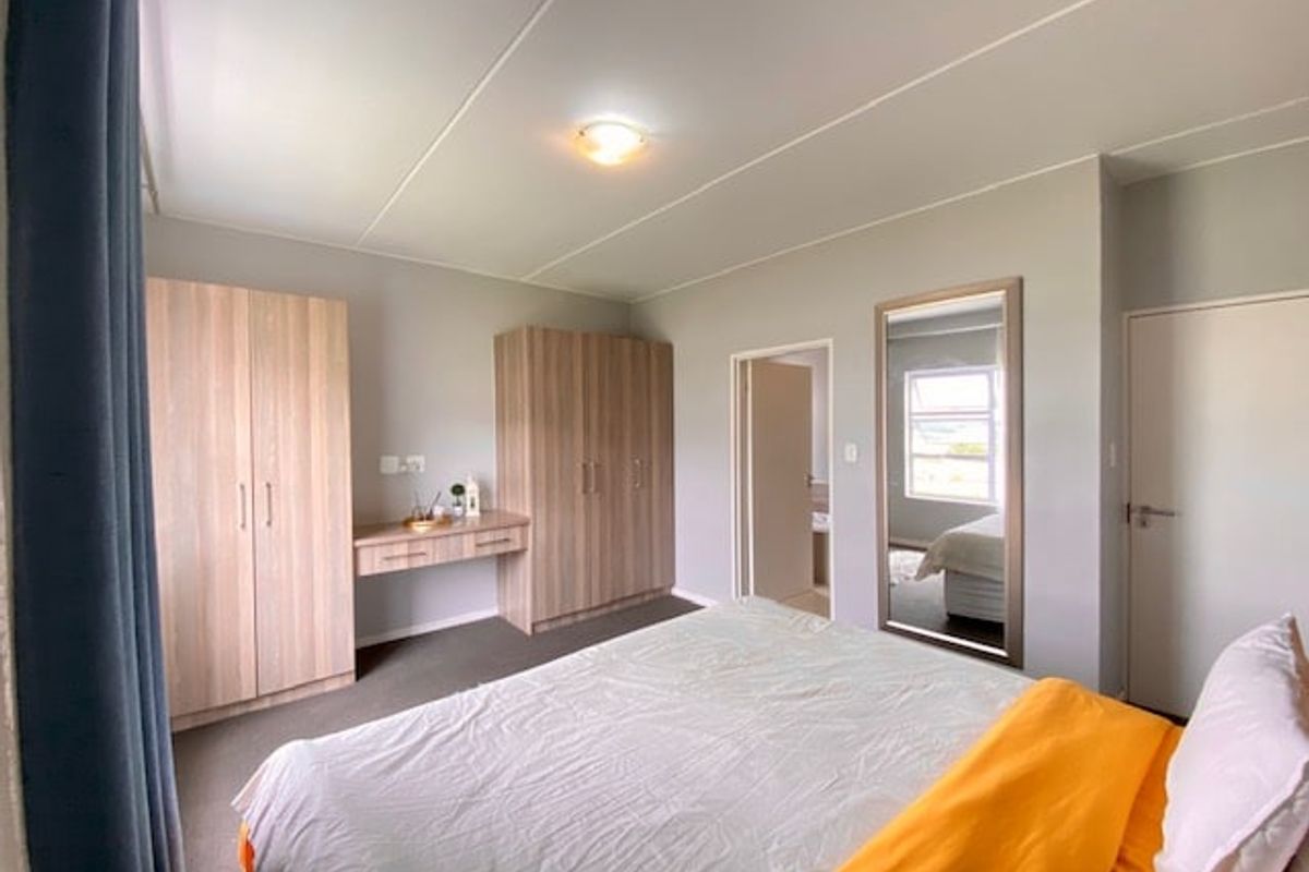 A well-maintained bedroom featuring built-in wooden cupboards with an integrated vanity unit, neutral wall finishes, and carpeted flooring.