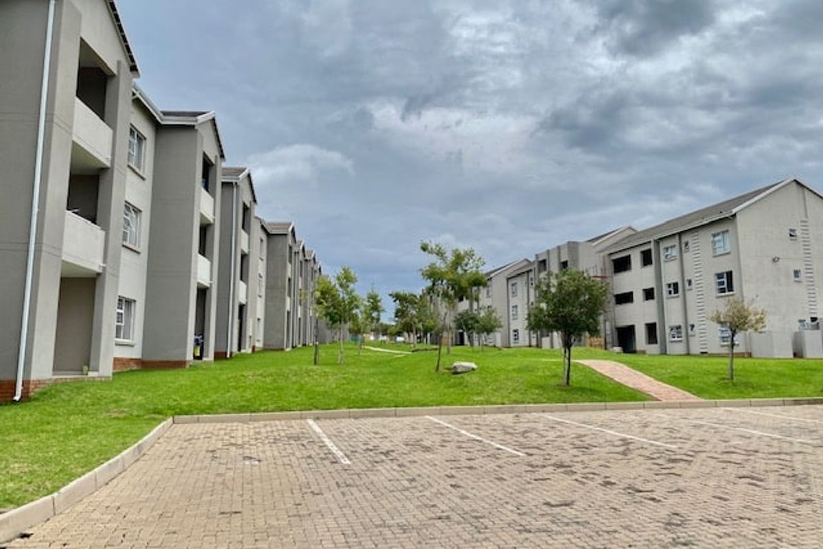 Exterior view of a multi-story apartment complex featuring paved parking, landscaped green spaces, and building facades with balconies.