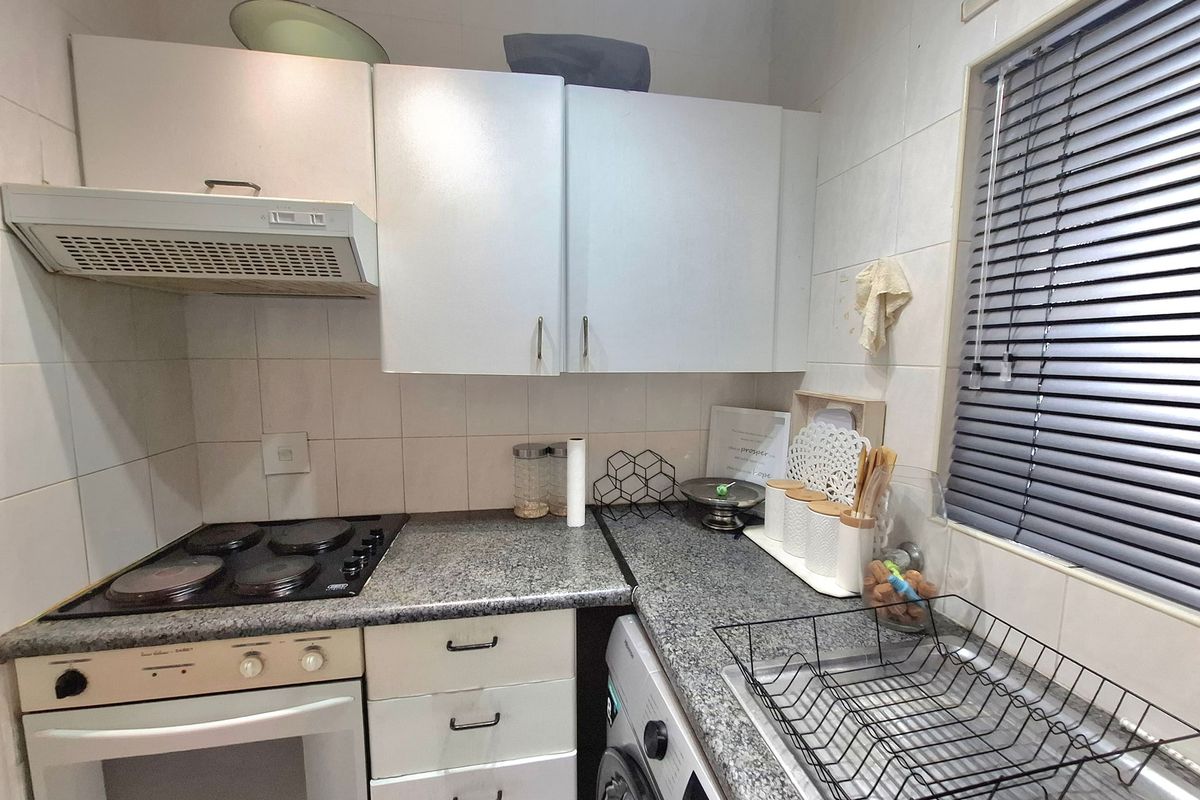 Compact kitchen featuring granite countertops, built-in electric hob and oven, extractor fan, and integrated cabinetry with a tiled backsplash.