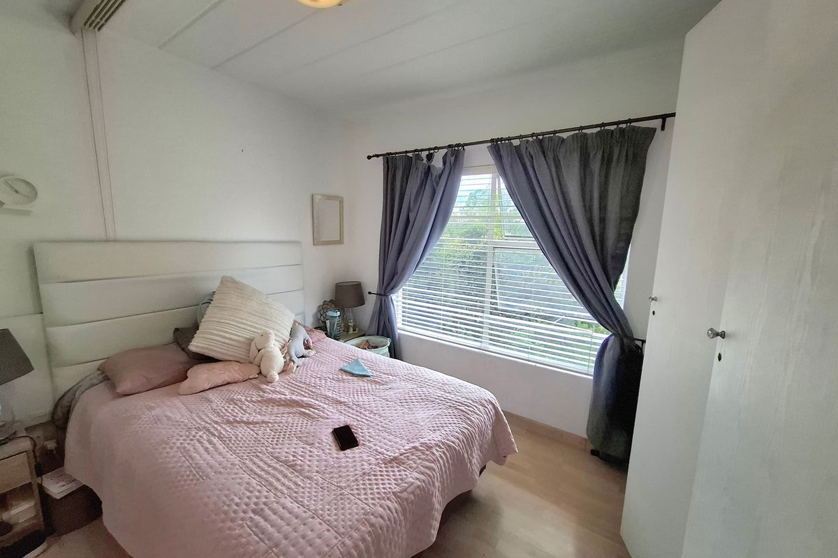 A functional bedroom featuring laminate flooring, a built-in wardrobe, and a window with fitted blinds and curtains.
