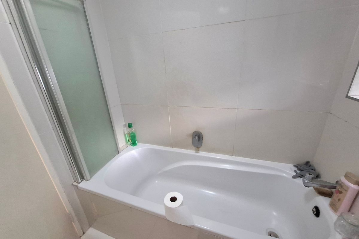 A functional bathroom featuring a standard bathtub with a glass shower screen and neutral wall tiling.