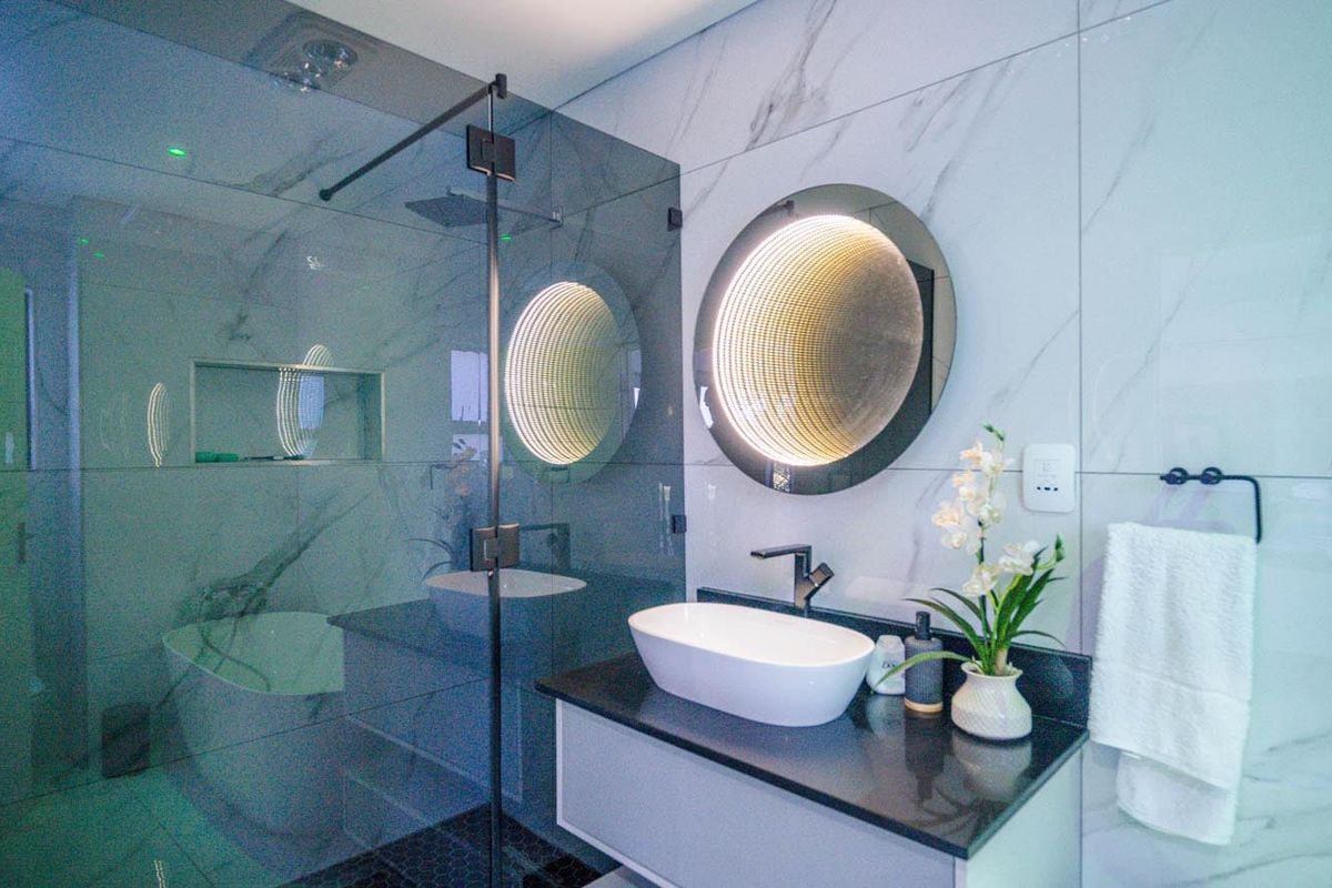 Modern bathroom featuring marble-look wall tiles, a floating vanity with a vessel sink, a glass shower enclosure, and a striking backlit infinity mirror.