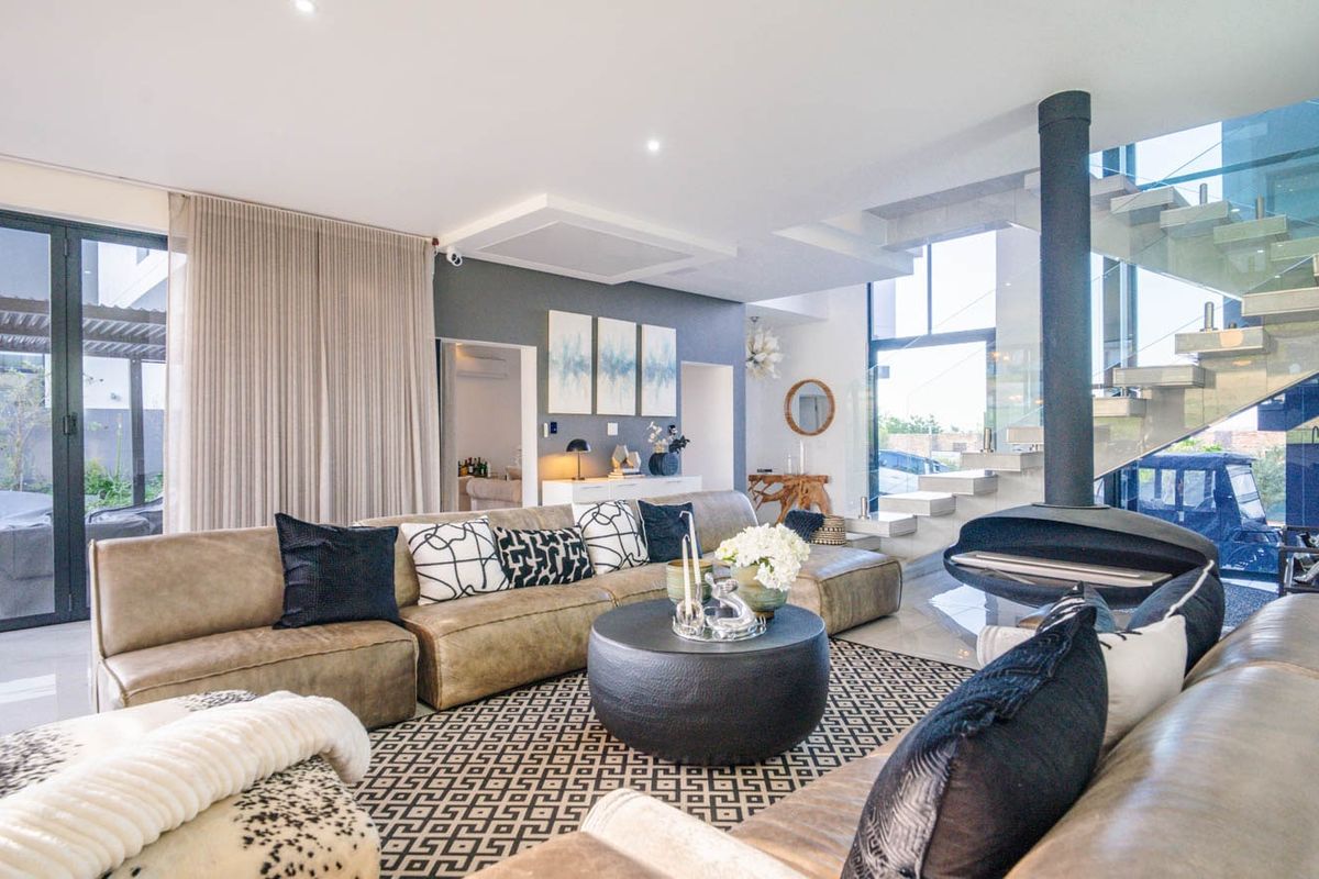 Modern open-plan living area featuring a striking suspended fireplace, floating staircase with glass balustrade, and large sliding doors leading to the patio.