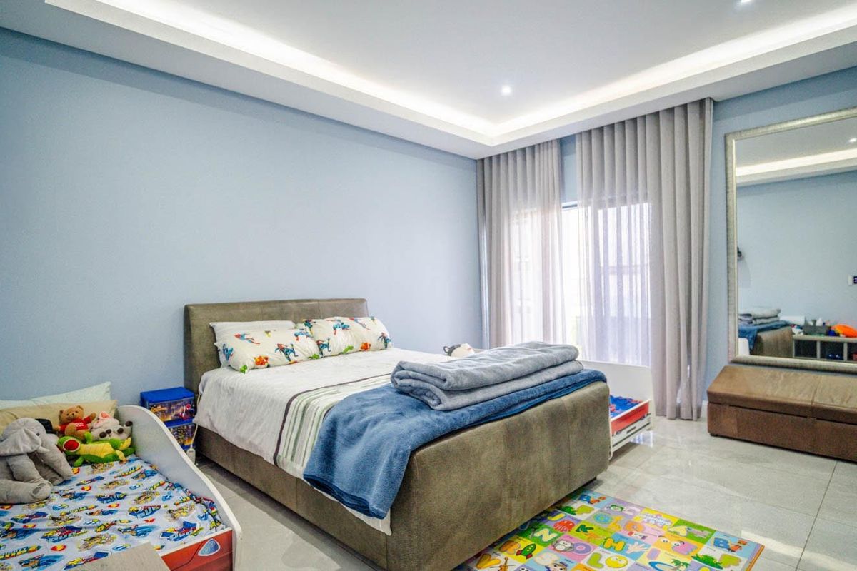 Spacious bedroom featuring modern recessed ceiling with cove lighting, large windows with floor-to-ceiling curtains, and neutral tiled flooring.