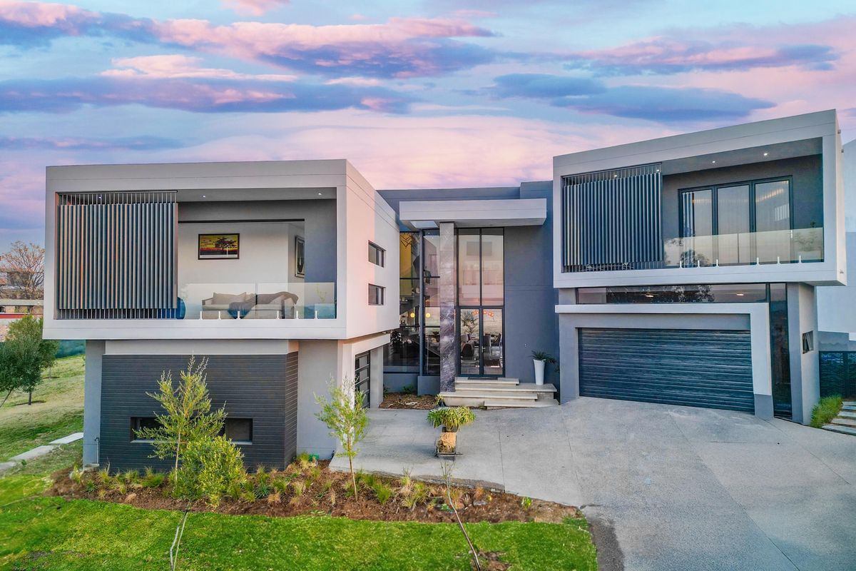 Modern double-story luxury residence featuring a contemporary facade, double garage, and spacious upper-level balcony with glass balustrades.