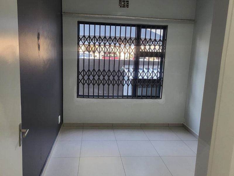 An empty bedroom featuring tiled flooring, a security gate on the window, and a dark accent wall.