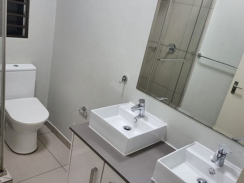 A clean, modern bathroom featuring a double vanity with vessel sinks, a large wall-mounted mirror, and neutral floor tiling.