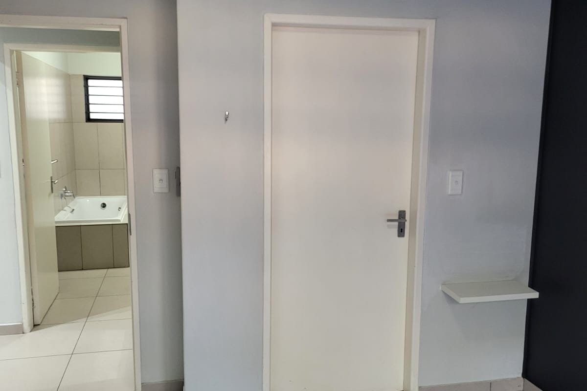 A clean, empty bedroom featuring neutral tiled flooring and a direct view into an adjoining bathroom with a built-in bathtub.