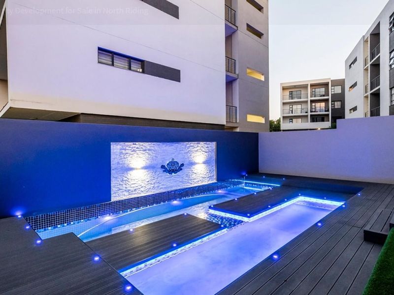 Modern apartment complex pool area featuring a contemporary swimming pool with integrated decking, feature wall, and ambient LED lighting.