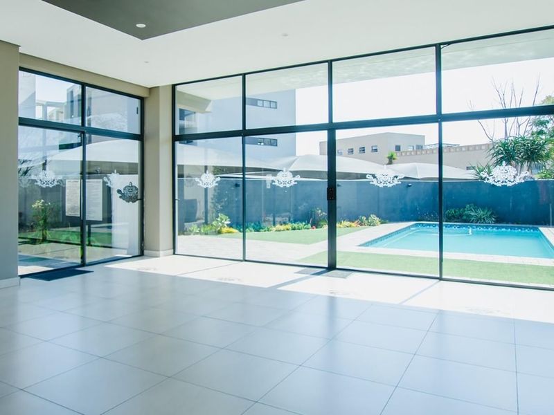 Spacious, light-filled living area featuring large-format floor tiles and expansive floor-to-ceiling windows with direct views of the swimming pool and garden.