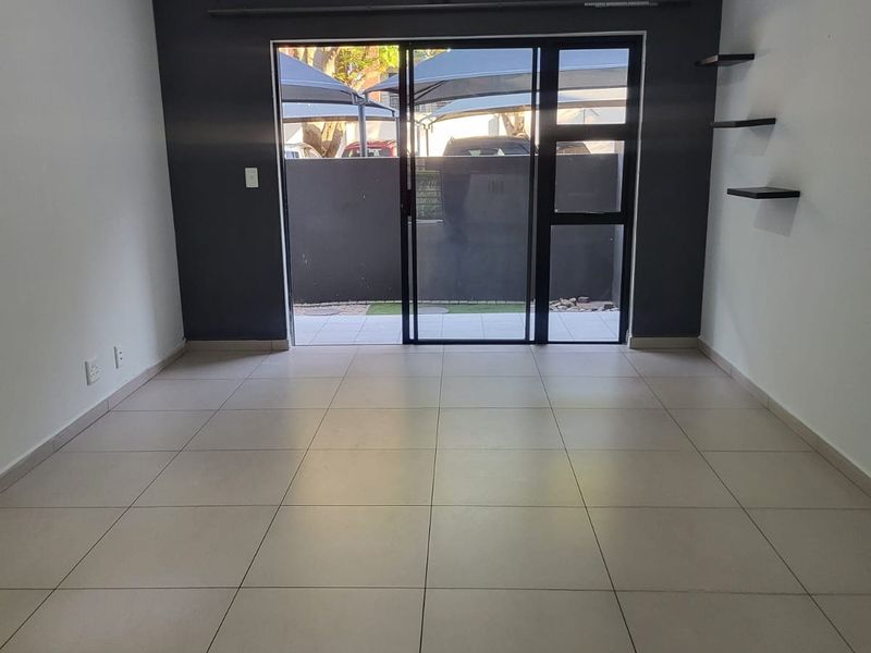 An empty living room featuring tiled flooring, a dark accent wall, and a sliding glass door providing access to the exterior.