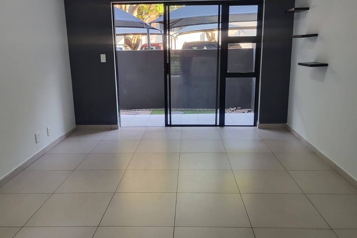 An empty living room featuring tiled flooring, a dark accent wall, and a sliding glass door providing access to the exterior.