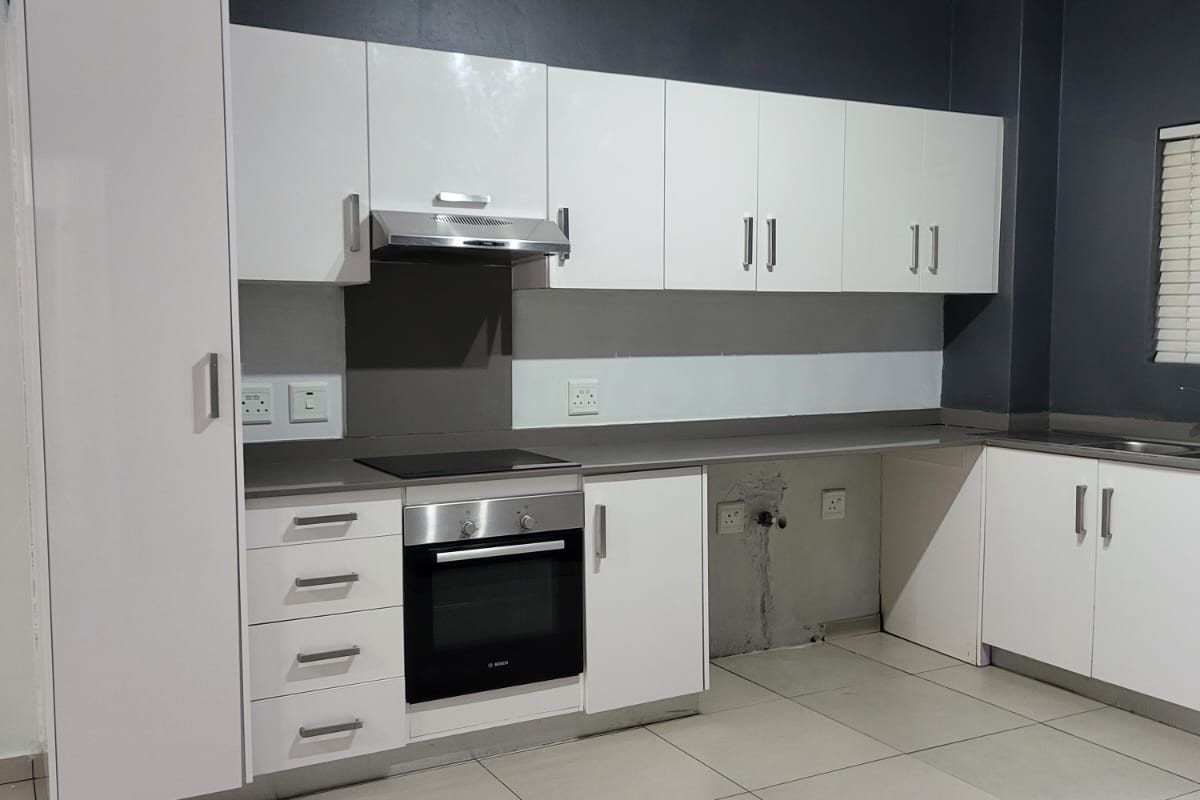Modern kitchen featuring white cabinetry, built-in oven and hob, extractor fan, and tiled flooring. The space includes a dedicated area for an under-counter appliance.