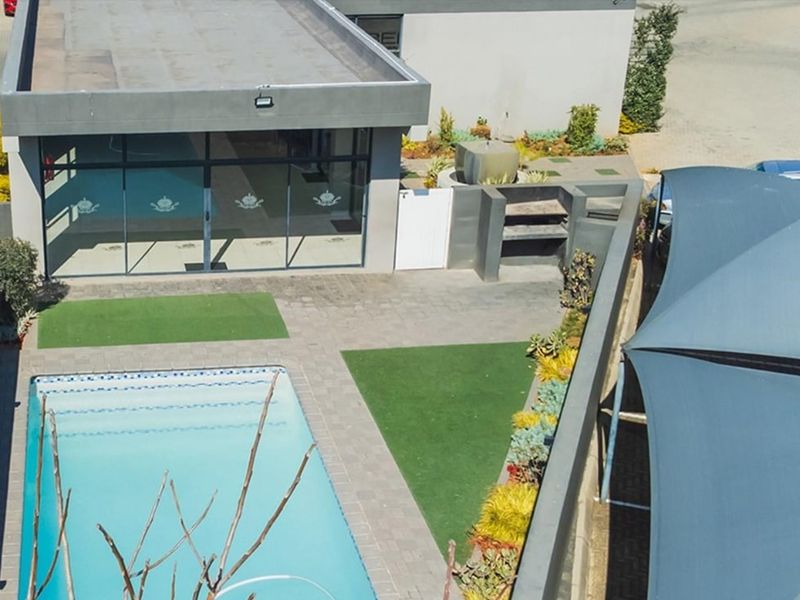 Aerial view of a modern apartment complex outdoor area featuring a swimming pool, built-in braai, paved patio, and shaded parking structure.