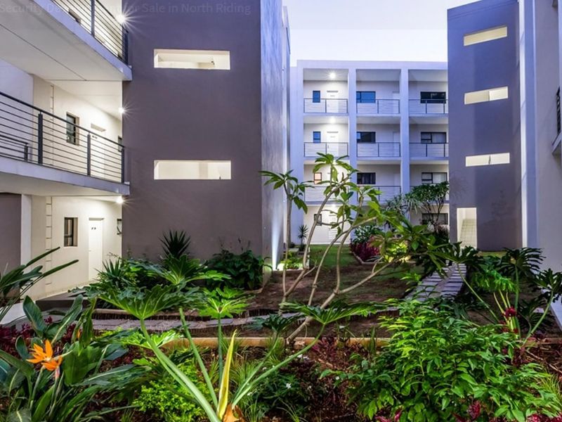 A well-maintained apartment complex courtyard featuring landscaped garden beds, paved pathways, and modern multi-story building facades with balcony access.
