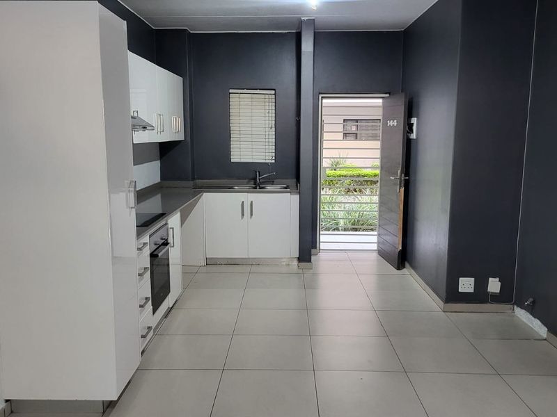 Modern open-plan kitchen featuring white cabinetry, built-in oven, hob, and tiled flooring, with direct access to the exterior through a secure entrance door.