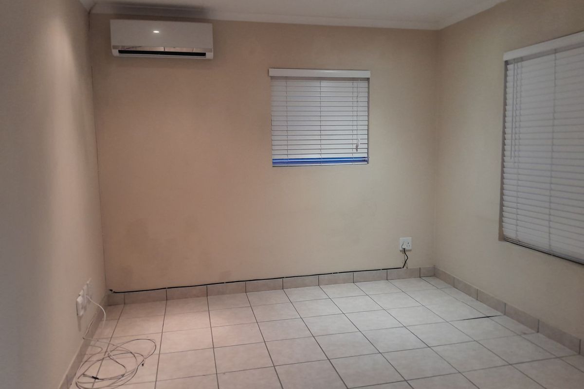 A clean, empty bedroom featuring tiled flooring, a wall-mounted split-system air conditioner, and venetian blinds on the windows.