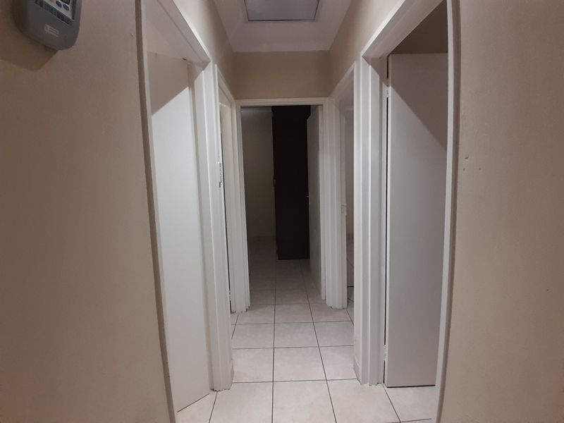 A neutral-toned hallway featuring tiled flooring and multiple internal door access points, providing a clean and functional transition space within the home.