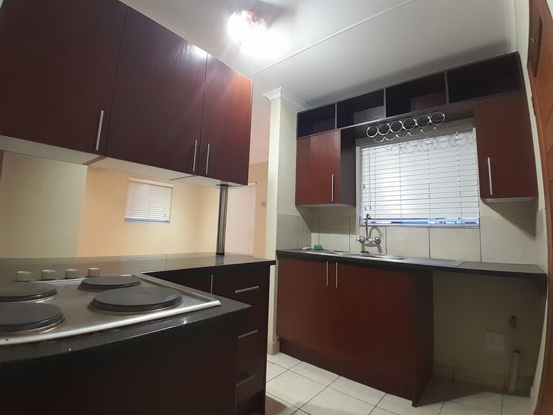 A functional kitchen featuring dark wood cabinetry, an electric hob, stainless steel sink, and tiled flooring, offering a clean and practical workspace.