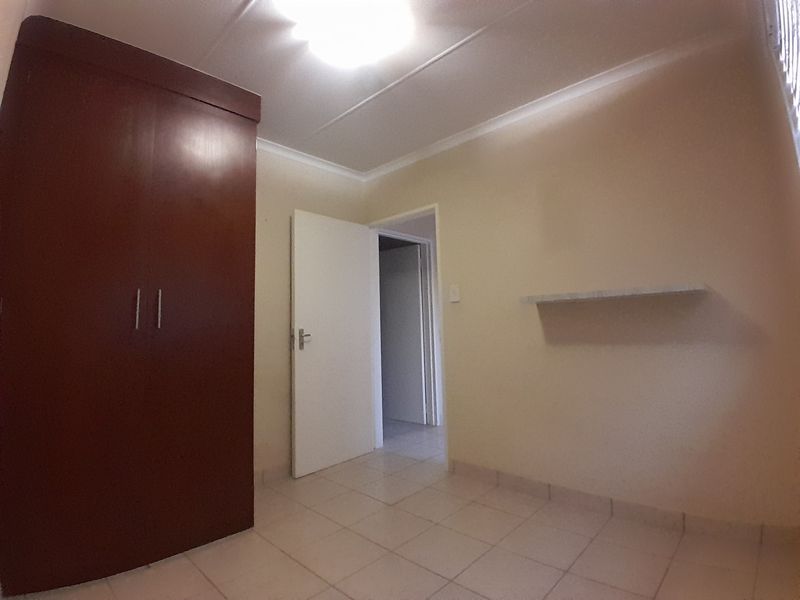 A simple, empty bedroom featuring tiled flooring, a built-in wooden wardrobe, and a wall-mounted shelf.