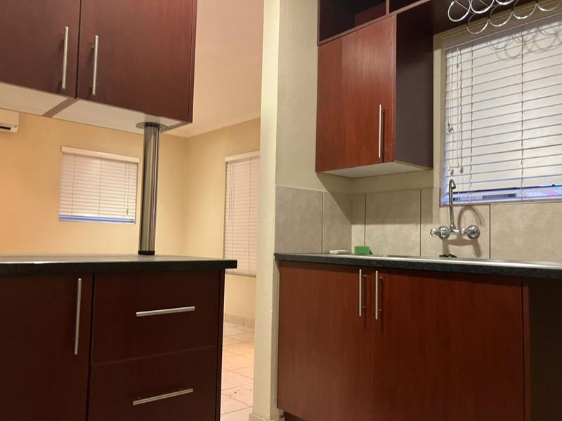A functional kitchen featuring dark wood cabinetry, laminate countertops, a stainless steel sink with chrome mixer tap, and tiled backsplash.