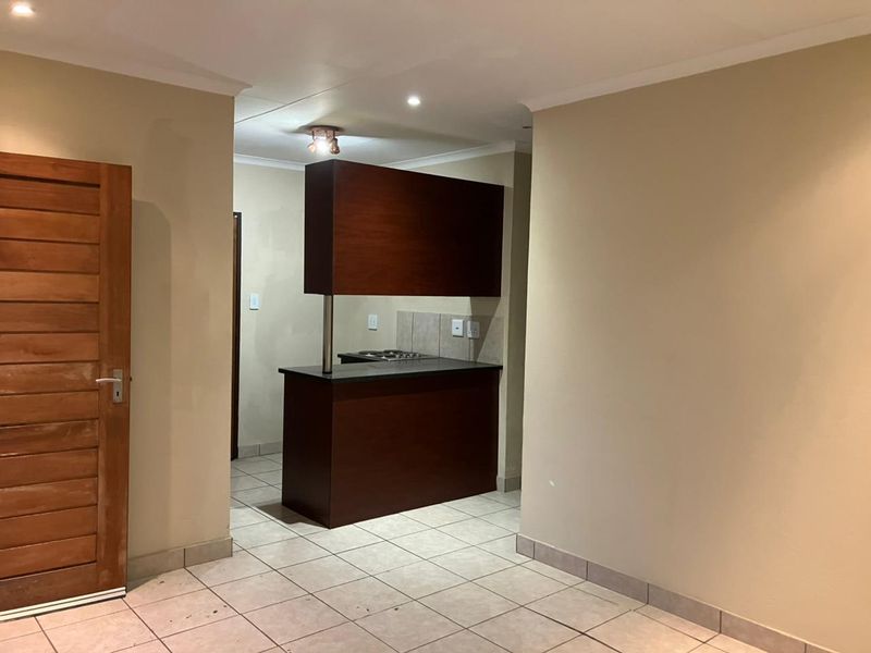 A compact kitchen area featuring dark wood cabinetry, a built-in hob, and tiled flooring, presenting a functional space ready for updates.