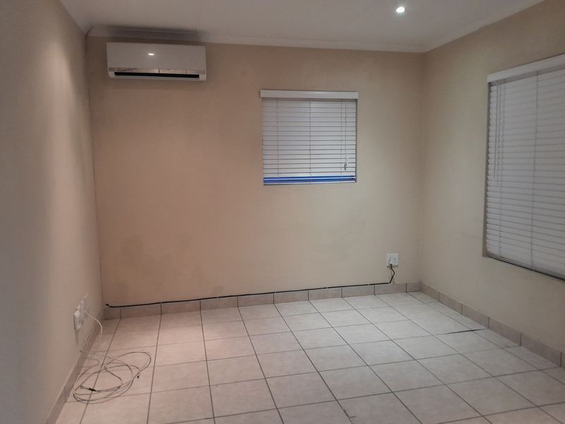 A clean, empty bedroom featuring tiled flooring, recessed lighting, venetian blinds, and a wall-mounted air conditioning unit.
