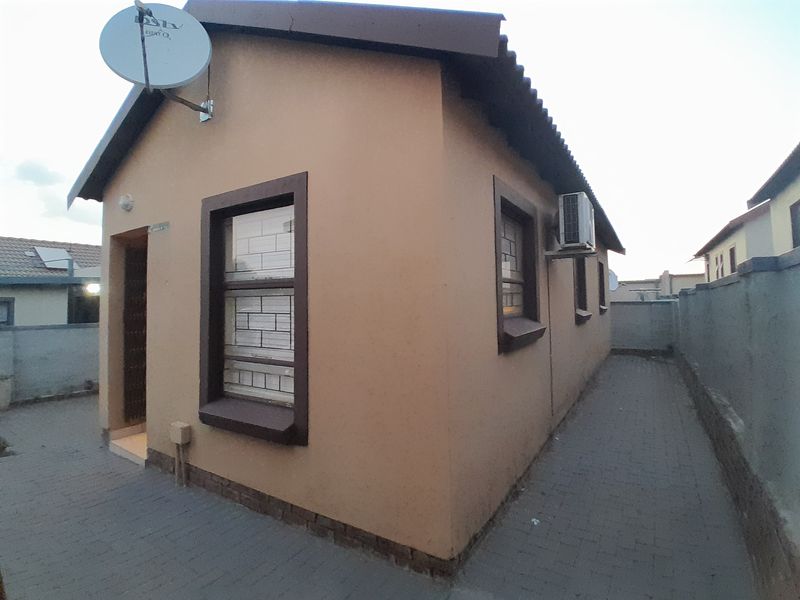Rear exterior view of the house featuring a paved walkway, boundary wall, and mounted air conditioning unit.