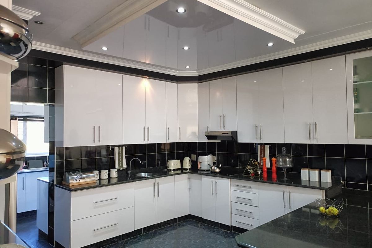 Modern kitchen featuring high-gloss white cabinetry, black granite countertops, a contrasting black tiled backsplash, and a recessed ceiling feature with integrated downlights.