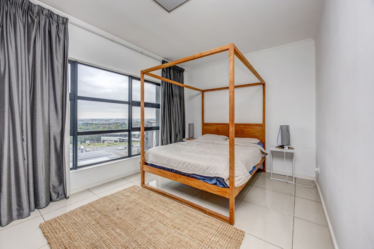 Spacious bedroom featuring large format floor tiles, expansive aluminium-framed windows with natural light, and a neutral interior finish.