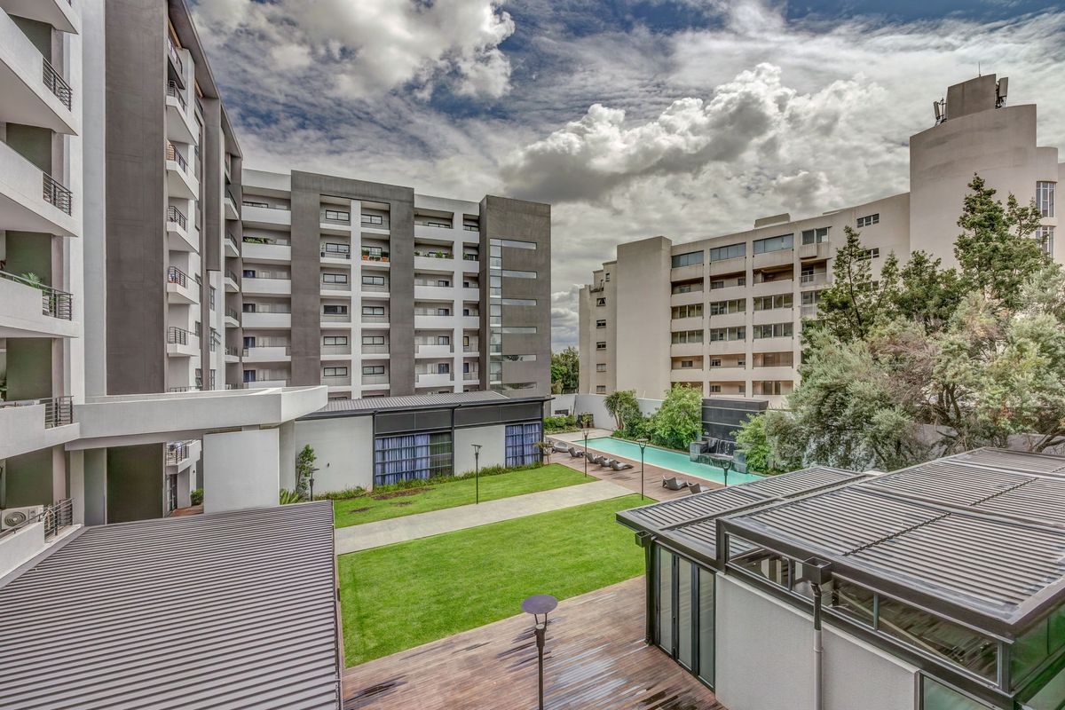 Elevated view of the apartment complex courtyard featuring a swimming pool, landscaped lawn, timber decking, and modern multi-story residential buildings.