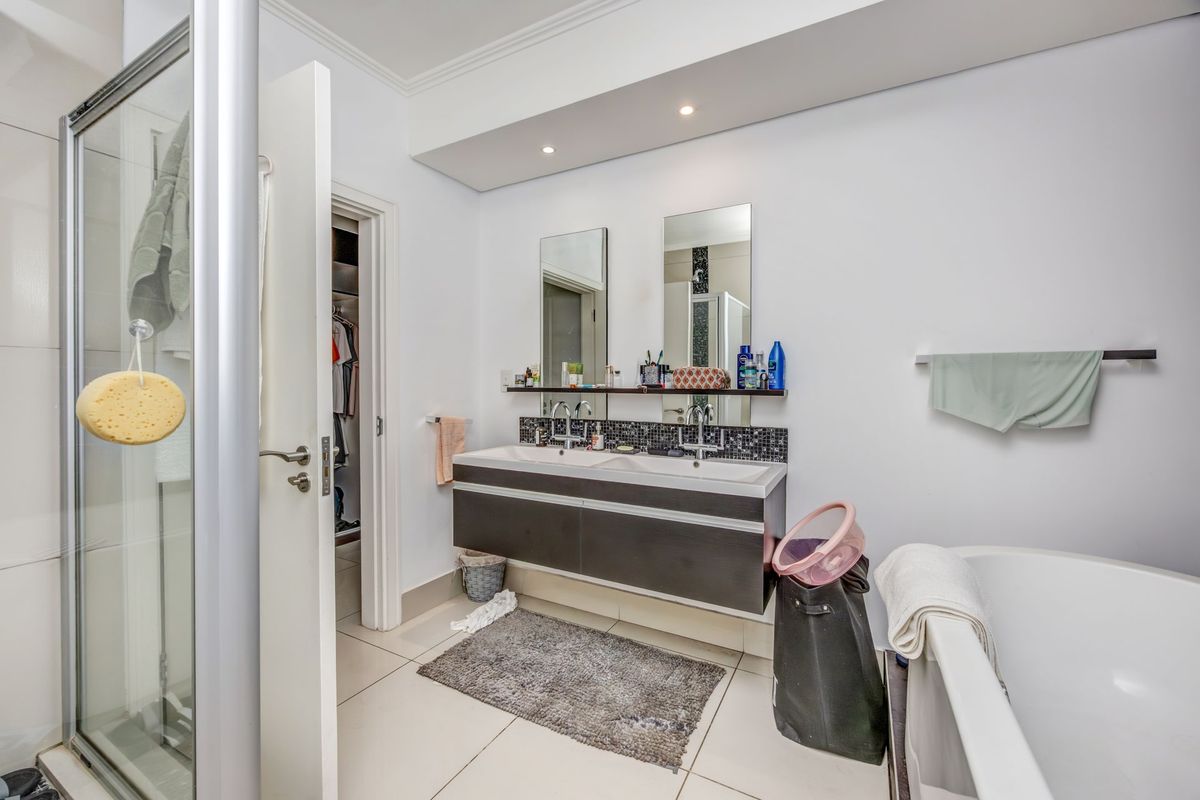 Modern bathroom featuring a double vanity with wall-mounted cabinetry, a glass shower enclosure, and a freestanding bathtub with recessed lighting.
