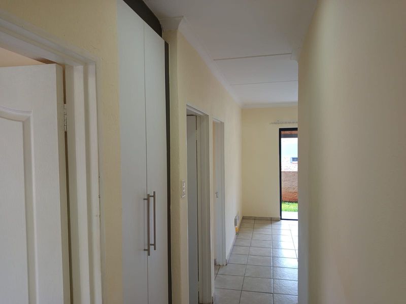 A clean, tiled hallway featuring built-in storage cupboards and access to adjacent rooms, leading towards an exterior doorway.