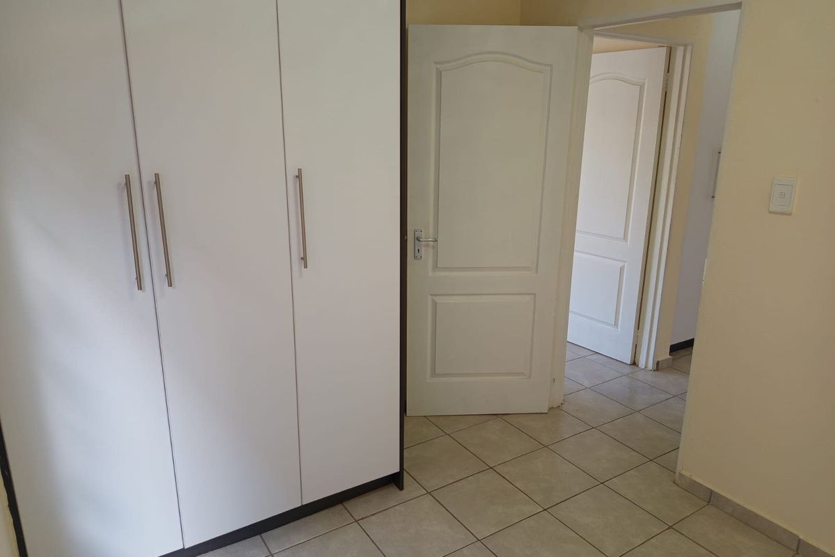 A clean, empty bedroom featuring white built-in wardrobes, neutral tiled flooring, and classic panel doors leading to adjacent rooms.
