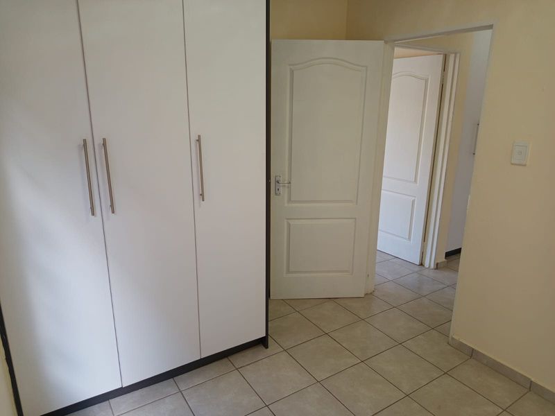 A clean, empty bedroom featuring white built-in wardrobes, neutral tiled flooring, and classic panel doors leading to adjacent rooms.