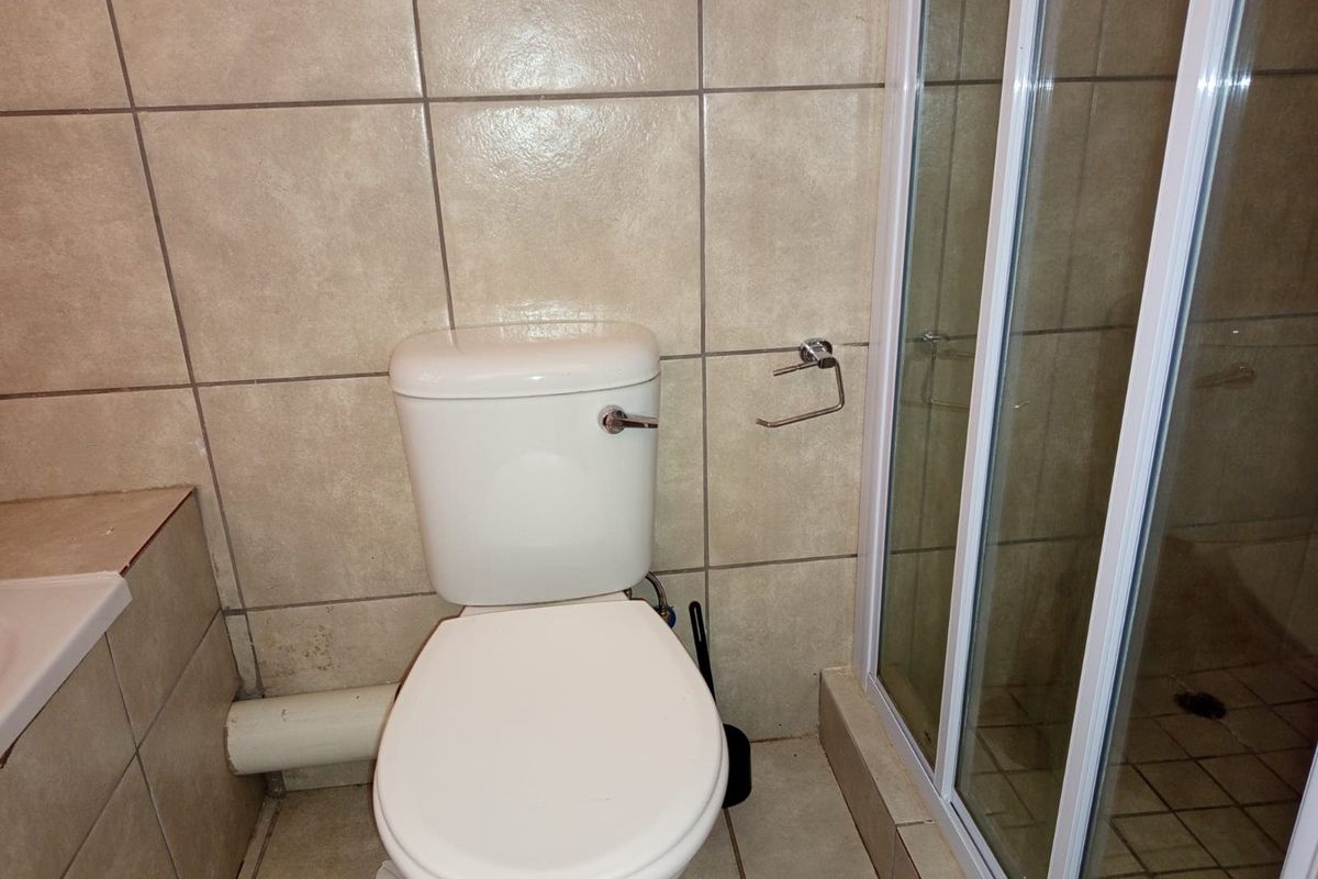 A functional bathroom featuring a standard toilet, shower enclosure, and neutral ceramic tiling throughout.