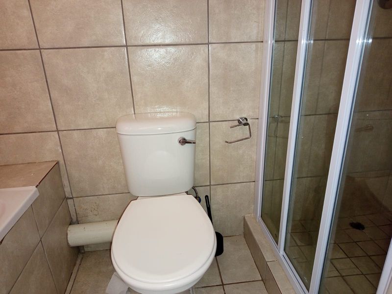 A functional bathroom featuring a standard toilet, shower enclosure, and neutral ceramic tiling throughout.
