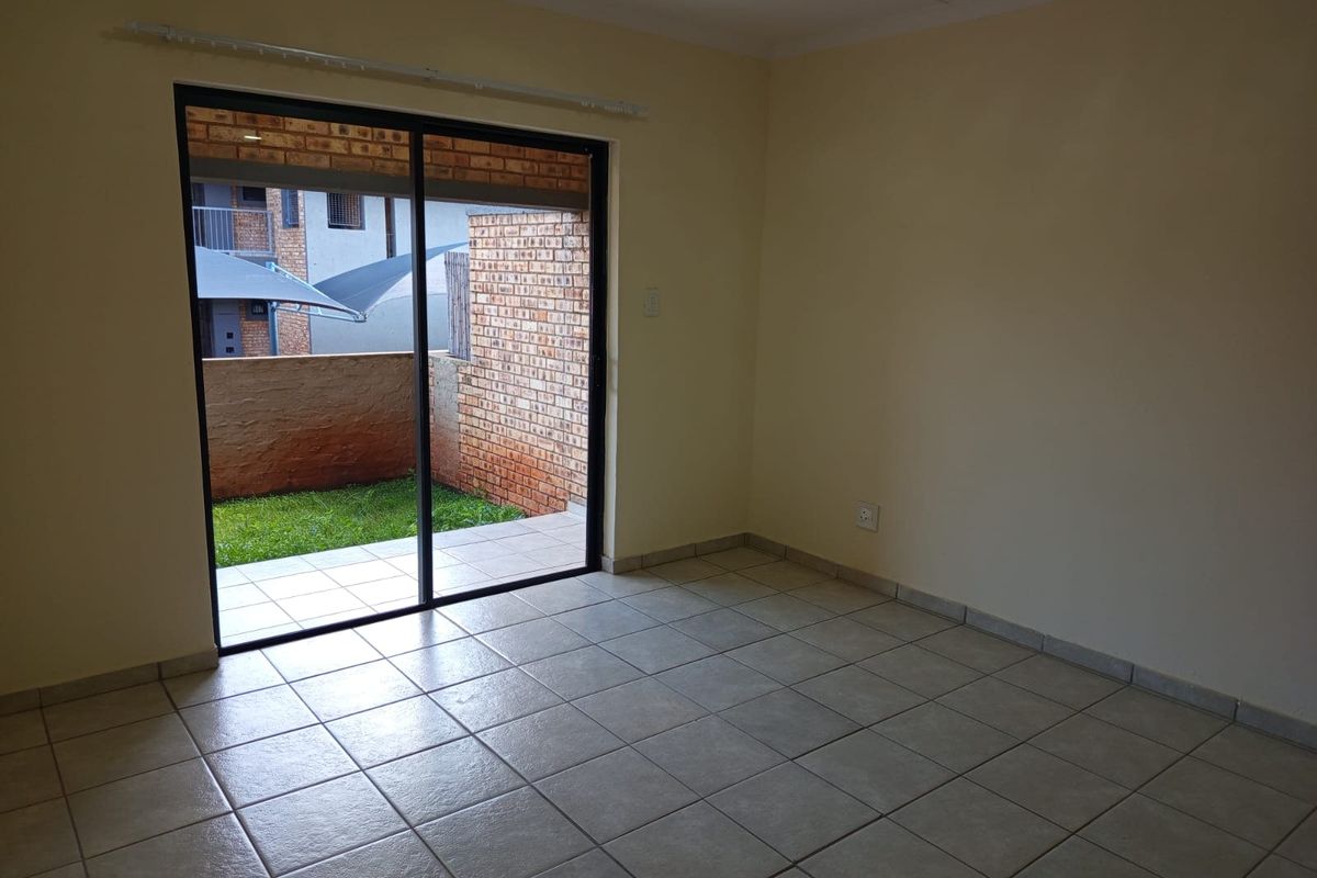 An empty living room featuring neutral ceramic floor tiles and a large sliding glass door providing direct access to an outdoor patio area.