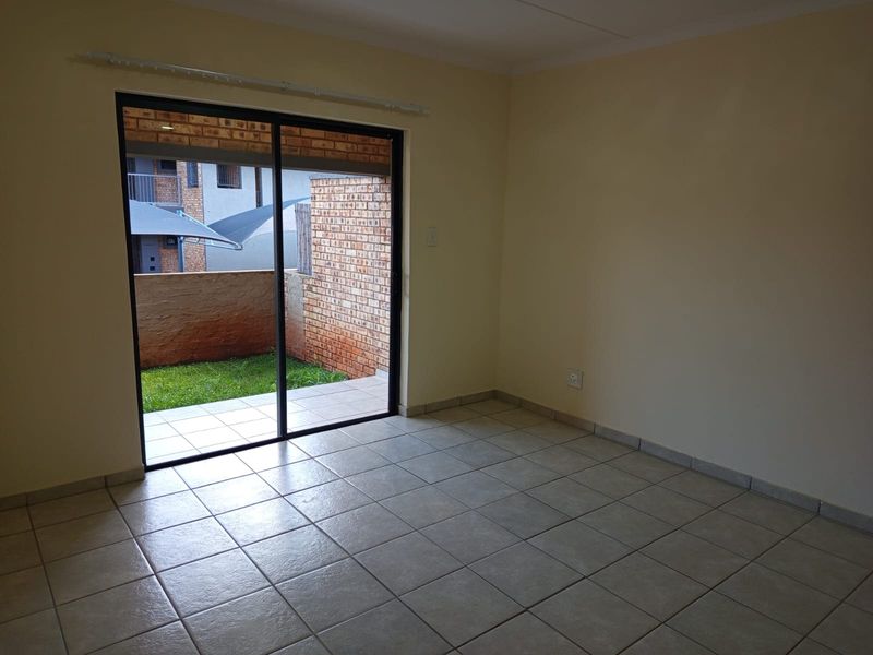 An empty living room featuring neutral ceramic floor tiles and a large sliding glass door providing direct access to an outdoor patio area.