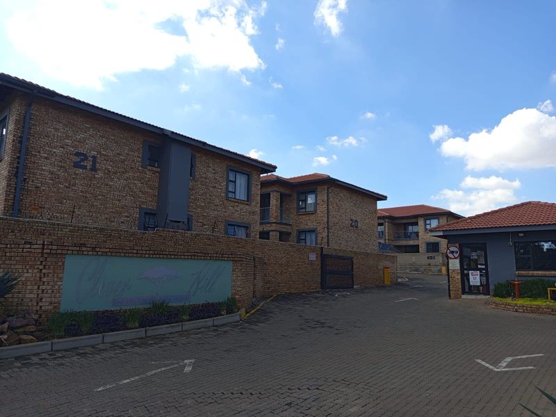 Exterior view of the Clover Hill apartment complex featuring face brick buildings, tiled roofs, and a paved entrance driveway with a security gatehouse.