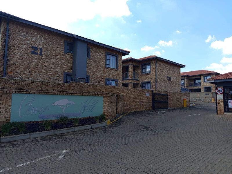 Exterior view of the Clover Hill apartment complex featuring face brick buildings, paved driveway access, and secure perimeter walling.